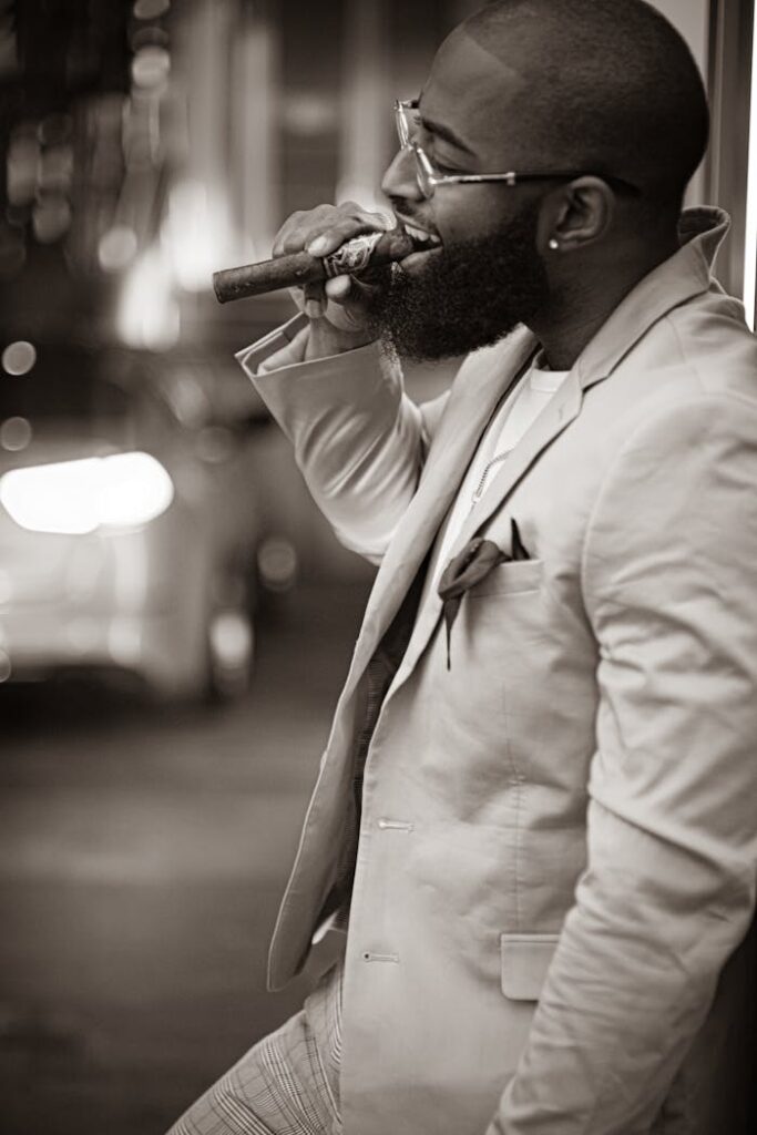 A fashionable man in a suit smokes a cigar at night, exuding confidence and style.