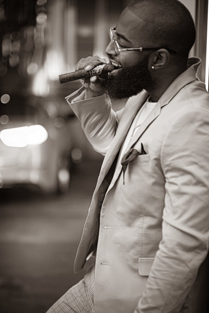 A fashionable man in a suit smokes a cigar at night, exuding confidence and style.